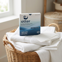 Box of otter laundry detergent sheets on folded white towels in a wicker basket.